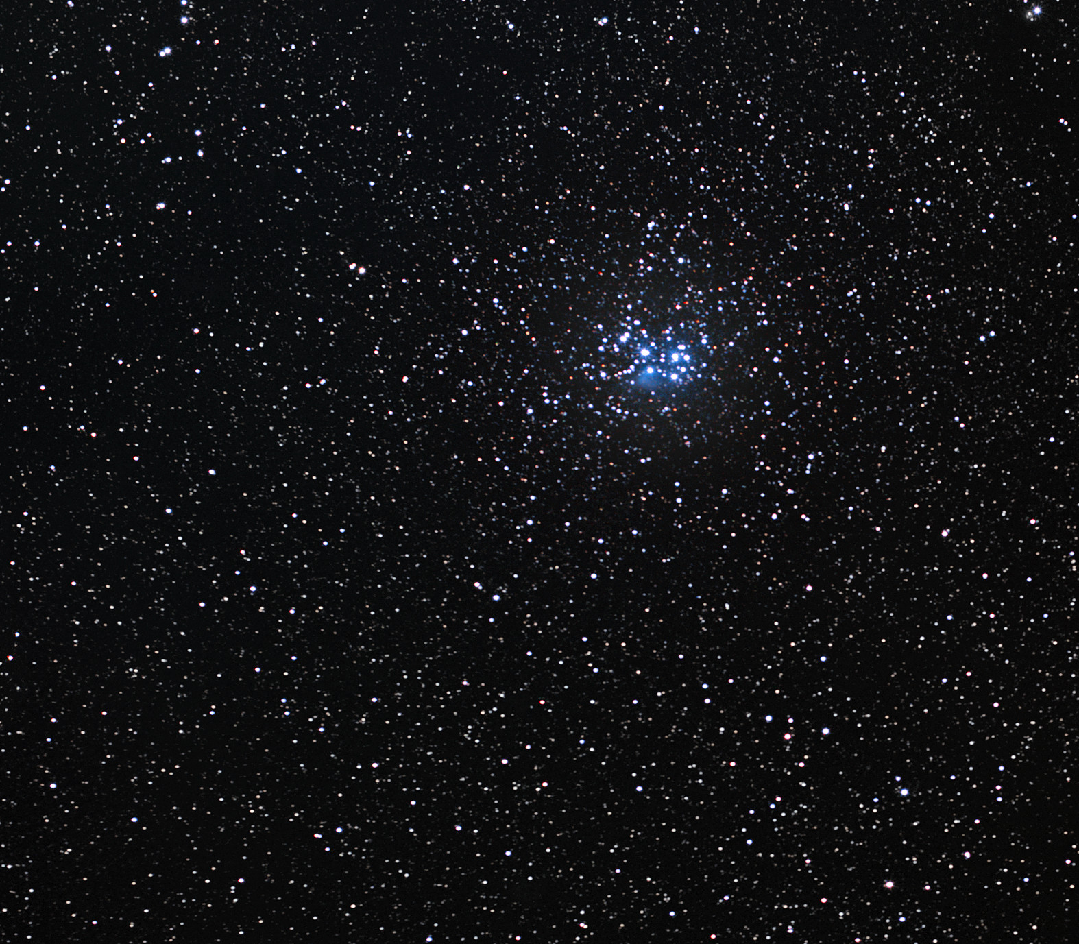 Real ground-based photograph of the Pleiades: a compact group of bright blue stars amid a much wider field of stars.